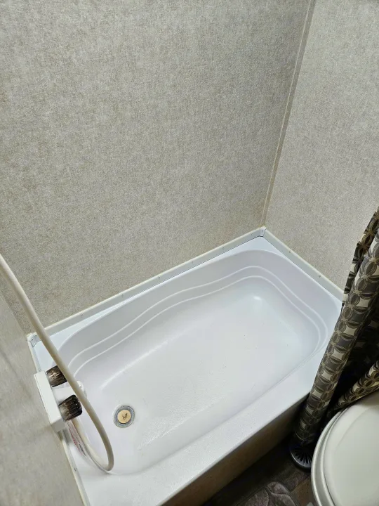 Compact shower and bathtub unit in an RV rental bathroom, featuring textured walls and a patterned shower curtain.. Jayco Jay Flight SLX 2019