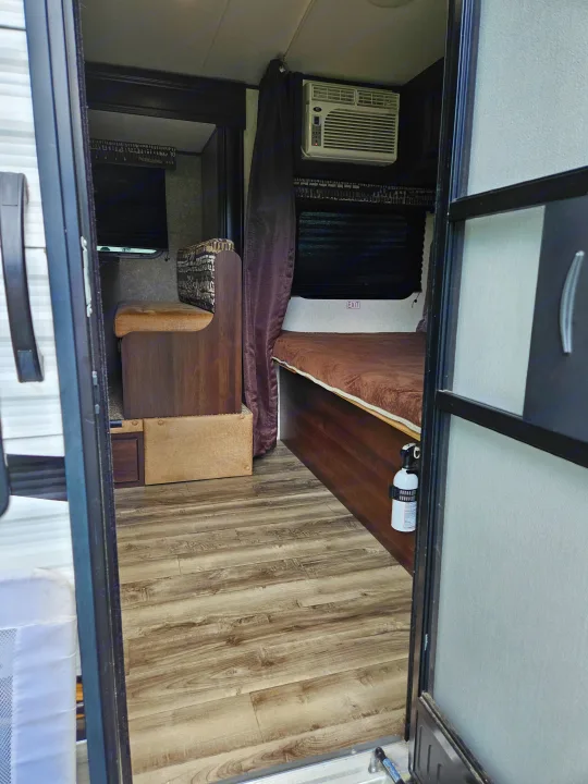 Cozy RV rental interior with a dinette, bed, AC unit, and fire extinguisher, viewed from the entry door.. Jayco Jay Flight SLX 2019