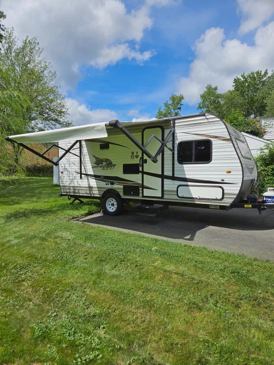 This Jay Flight SLX RV rental, a travel trailer with an extended awning, is parked on green grass under a blue sky.. Jayco Jay Flight SLX 2019