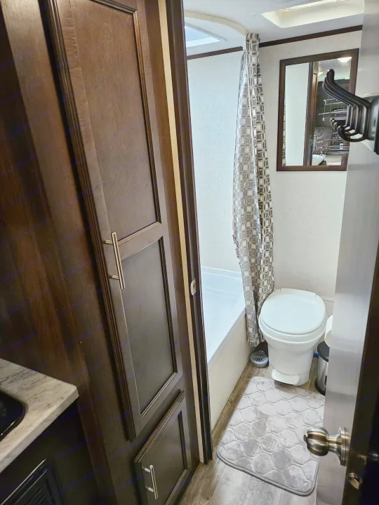 Compact RV rental bathroom with shower, toilet, and storage, featuring dark wood cabinets and a light interior.. Jayco Jay Flight SLX 2019