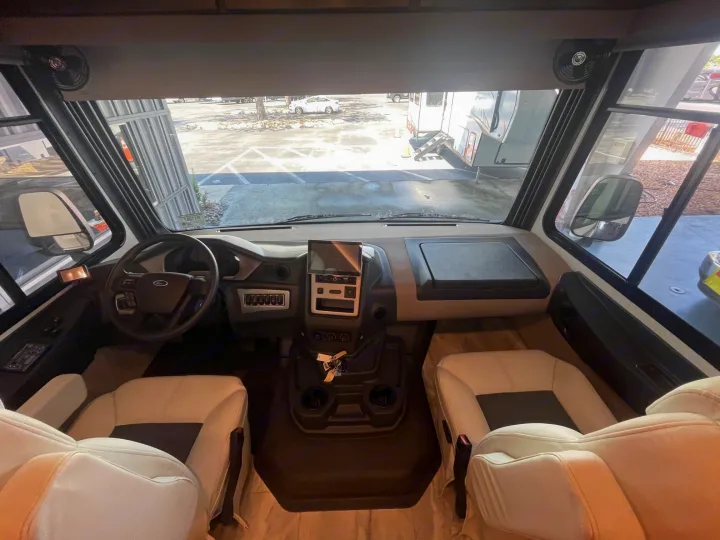 Inside a modern RV rental, showing the driver's cockpit, cream seats, dashboard with screen, and parking lot view.. Coachmen MIRADA 35ESF 2026