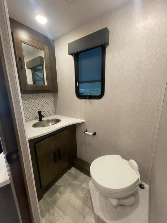 Modern RV rental bathroom with a white toilet, dark wood vanity, sleek sink, mirror, and patterned backsplash.. Coachmen MIRADA 35ESF 2026
