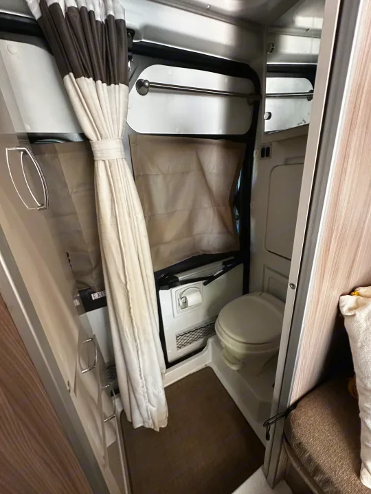 This rv rental wet bath features a compact shower and toilet area with a brown curtain, towel bar, and floor mat.. Thor Sequnce 2023