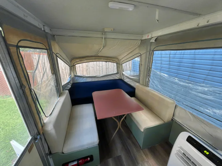 Inside a pop-up camper RV rental: a cozy dinette, large bed, and portable AC unit create a functional interior.. Coleman Destiny Cedar 1992