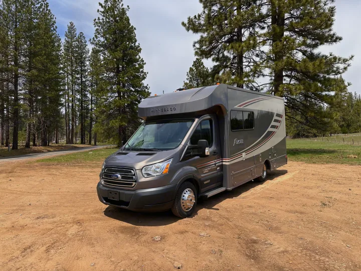Grey Winnebago Fuse rv rental in a rustic setting, surrounded by tall pine trees. Ideal for camping & road trips.. Winnebago Fuse 2017
