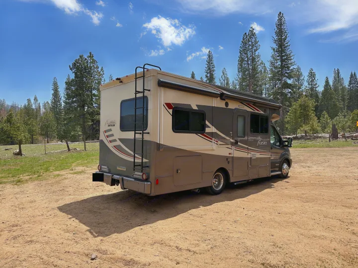 RV rental parked in a forest clearing under a blue sky, perfect for outdoor adventures and camping trips.. Winnebago Fuse 2017