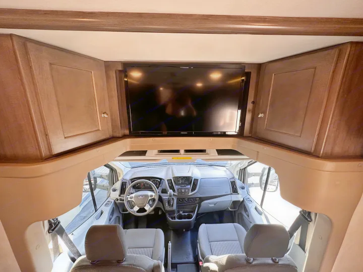 Spacious rv rental interior: View of the cockpit with steering wheel, dashboard, front seats, and an overhead TV.. Winnebago Fuse 2017