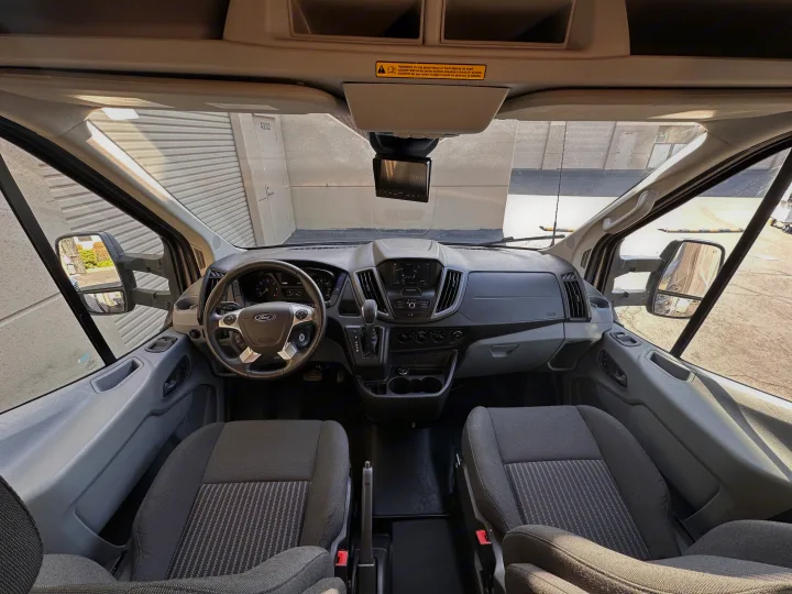 Looking forward from inside this rv rental van, the cockpit shows a Ford steering wheel, dashboard, and front seats.. Winnebago Fuse 2017
