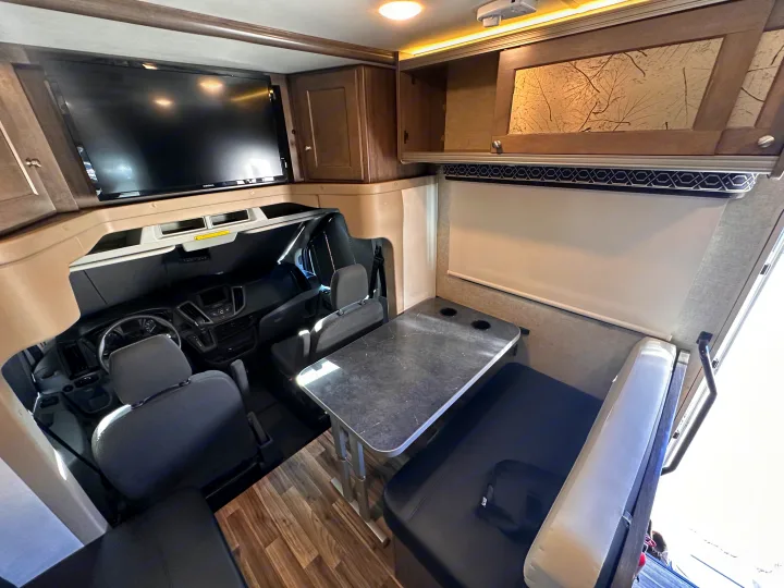Inside this RV rental: a cozy dinette with a dark table, overhead storage, TV, and the integrated driver's cabin.. Winnebago Fuse 2017