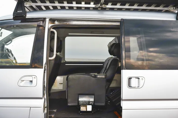 Inside view of a silver RV rental van with the sliding door open, showing comfortable seating and an ocean view.. Mitsubishi Delica 2005