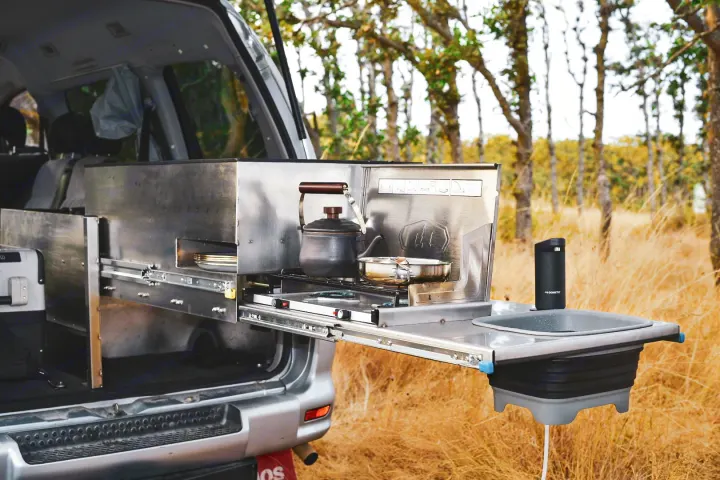 Rear of an RV rental with pull-out stainless steel camp kitchen. Features stove, kettle, pot, and sink setup.. Mitsubishi Delica 2005