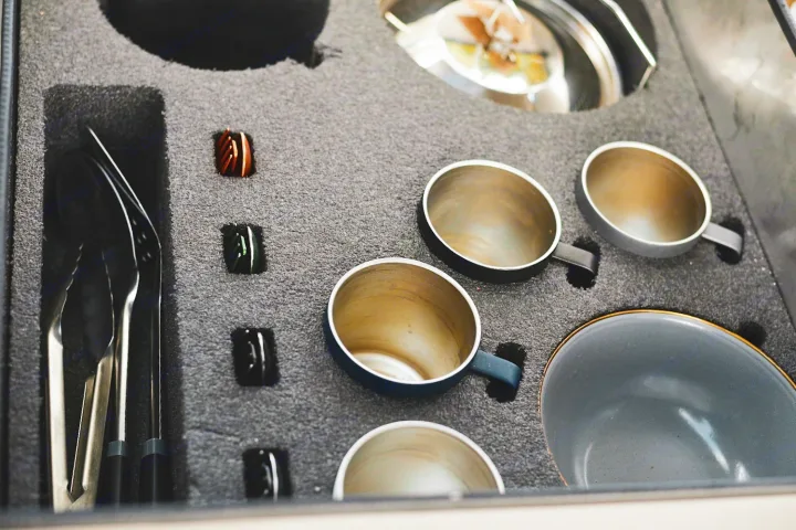 Organized RV rental kitchen essentials: stainless steel utensils, insulated mugs, and a bowl in custom foam storage.. Mitsubishi Delica 2005