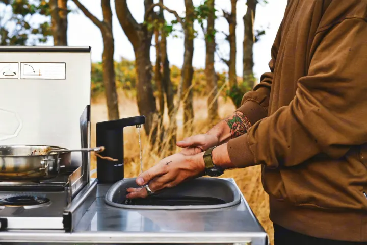 Washing up at a portable outdoor kitchen, ideal for your RV rental adventure. Enjoy camping convenience in nature.. Mitsubishi Delica 2005