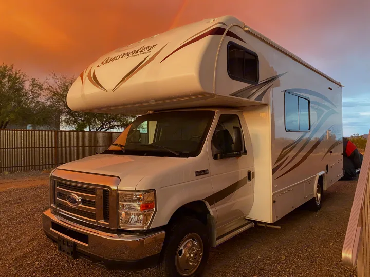 Sunseeker motorhome RV rental, white and bathed in a dramatic sunset glow with a faint rainbow, ready for travel.. Forest River Sunseeker 2017