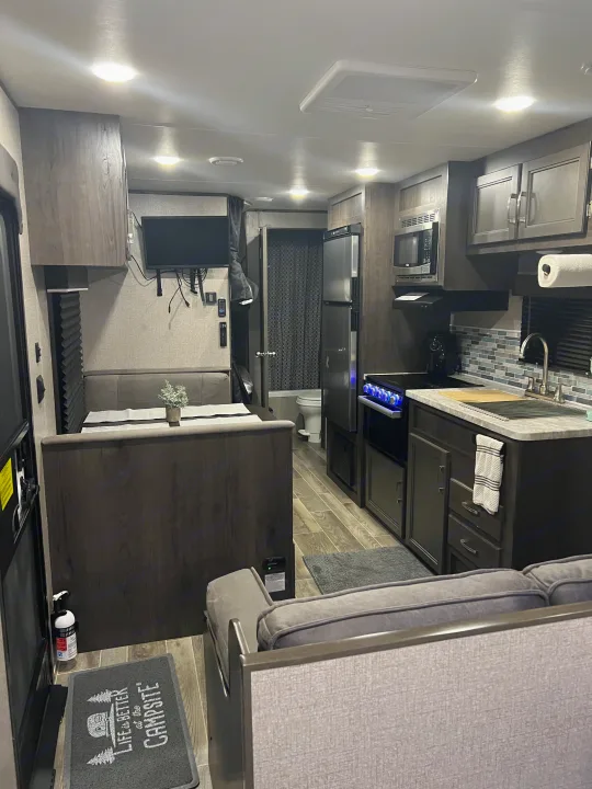 This RV rental interior features a modern kitchen, dining booth, sofa, and bathroom access. Brightly lit and functional.. Jayco Jay Flight SLX 2021