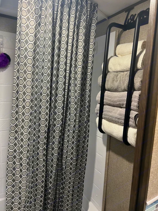 Clean RV rental bathroom showing a grey geometric shower curtain, purple loofah, and organized stacked towels.. Jayco Jay Flight SLX 2021
