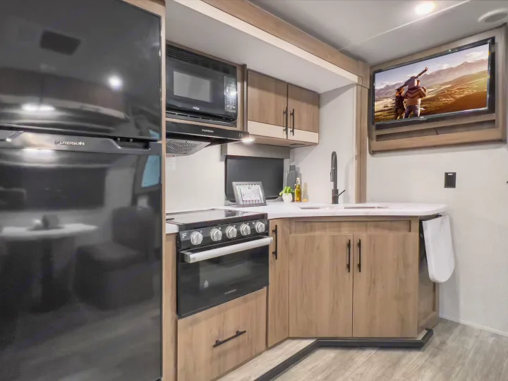 Spacious RV rental kitchen with modern appliances like a large fridge, microwave, stove, sink, and TV for comfortable living.. Grand Design Imagine XLS 2023