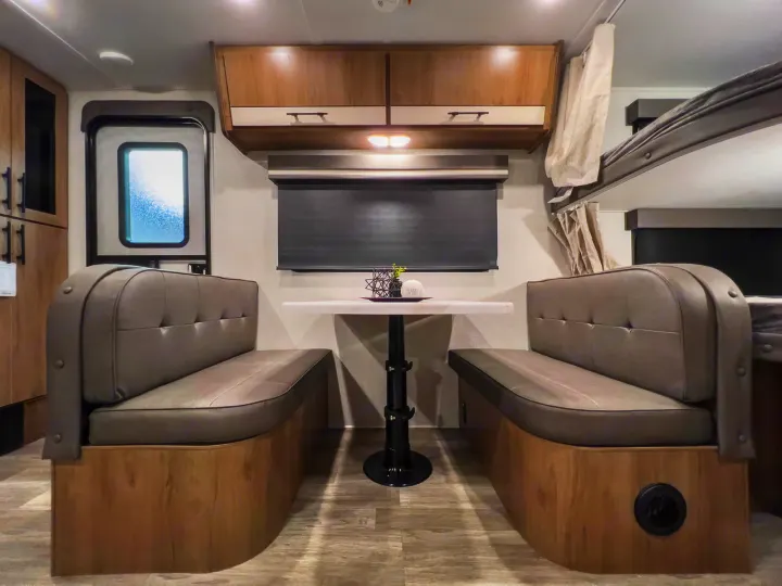RV rental interior showing a dinette with table & benches, overhead cabinets, window, & bunk beds.. Grand Design Imagine XLS 2023