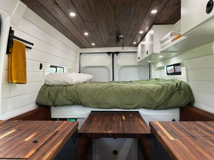 Inside this modern RV rental: a comfortable bed, wooden ceiling, and ample counter space for travel adventures.. RAM ProMaster 2500 2022