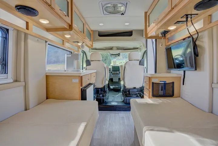 Bright RV rental interior: view of front from rear, showing opposing bench beds, kitchen w/ coffee maker, and TV.. Coachman Nova 20RB 2023
