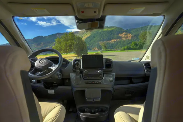 Driver's perspective inside an RV rental, showing the dashboard, steering wheel, and a vast mountain vista.. Coachman Nova 20RB 2023