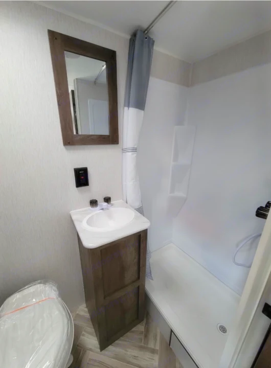 Compact RV rental bathroom featuring a vanity, sink, mirror, toilet (covered), & shower with built-in shelves.. Forest River Salem 2022