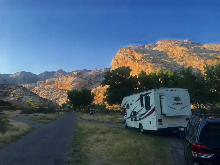 A large white Jayco rv rental is parked with a black car at a rustic campsite, framed by towering, light-colored mountains.. Jayco Redhawk 2017
