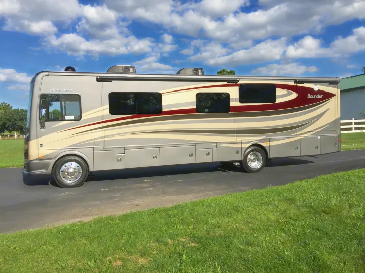 Modern Fleetwood Bounder RV rental parked on asphalt, lush grass, under a blue, cloudy sky. Ready for your adventure.. Fleetwood Bounder 2017