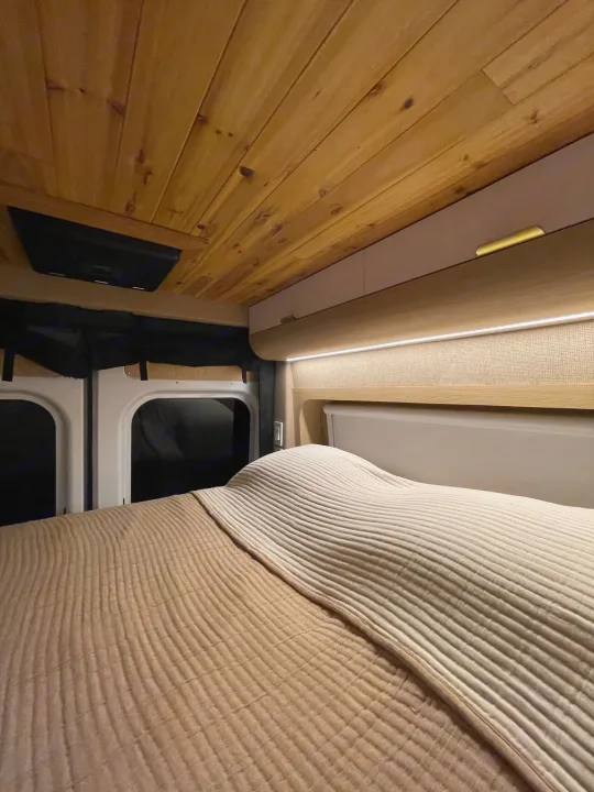 Experience comfort in this RV rental's cozy sleeping area, with a plush bed, wood ceiling, and ambient LED lighting.. Dodge Ram Promaster 3500 C/V HR 159 EXT 2023