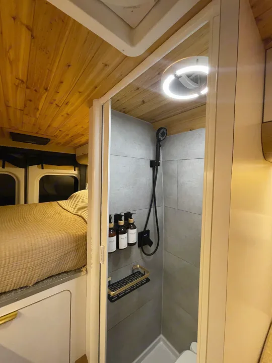 Inside this RV rental: a comfortable bed and a sleek, compact shower with grey tiles & black fixtures. Efficient space design.. Dodge Ram Promaster 3500 C/V HR 159 EXT 2023