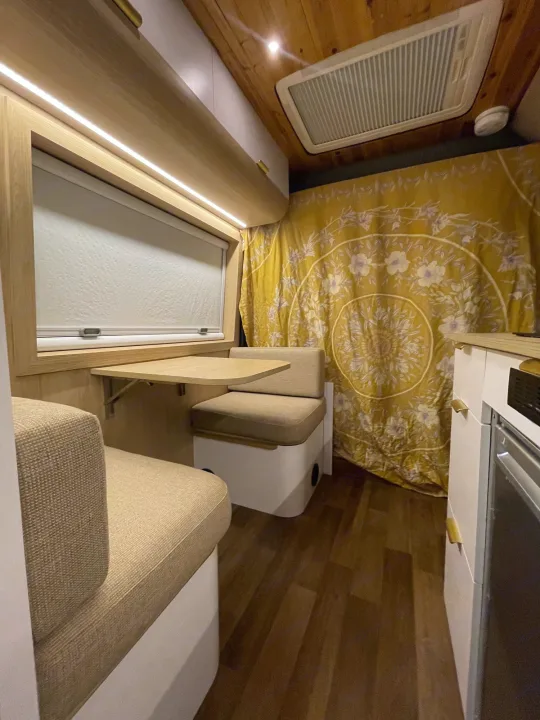 Explore this RV rental's cozy dinette with a foldable table, window, and vibrant yellow tapestry.. Dodge Ram Promaster 3500 C/V HR 159 EXT 2023
