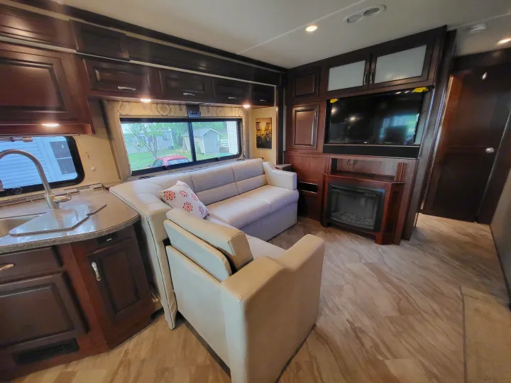 An inviting RV rental interior showcasing a cozy living area with sofa, TV, fireplace, and a functional kitchen.. Fleetwood Bounder 2017