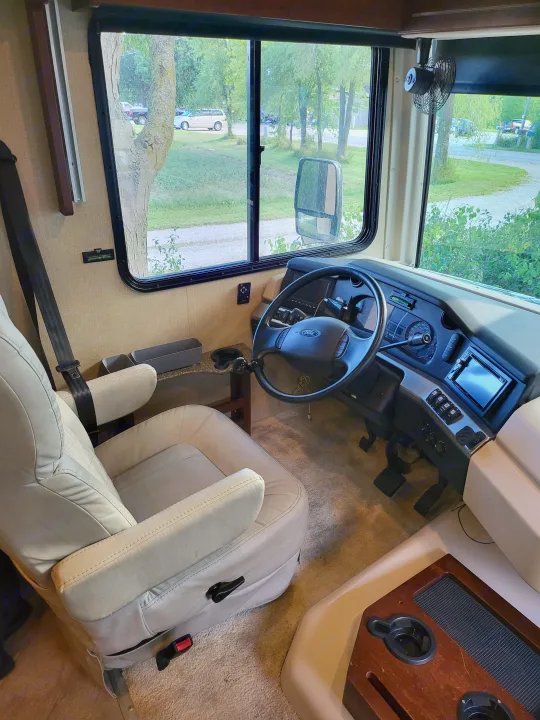 Driver's perspective inside an RV rental: cockpit with Ford steering wheel, comfortable seat, and view of the campsite.. Fleetwood Bounder 2017