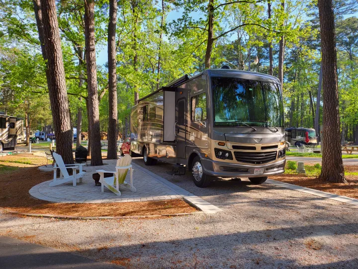 Spacious RV rental parked at a tranquil, tree-lined campsite with outdoor seating, perfect for a relaxing getaway.. Fleetwood Bounder 2017