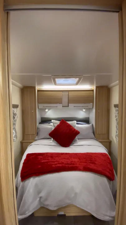 This compact RV rental bedroom offers a comfortable bed with grey linens & red accents, plus overhead storage.. Bailey Pheonix 640 2022