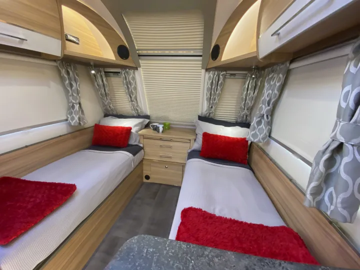 Step inside a comfortable rv rental sleeping area! This caravan interior features two single beds with red accents, a nightstand, and overhead storage.. Bailey Pheonix 640 2022