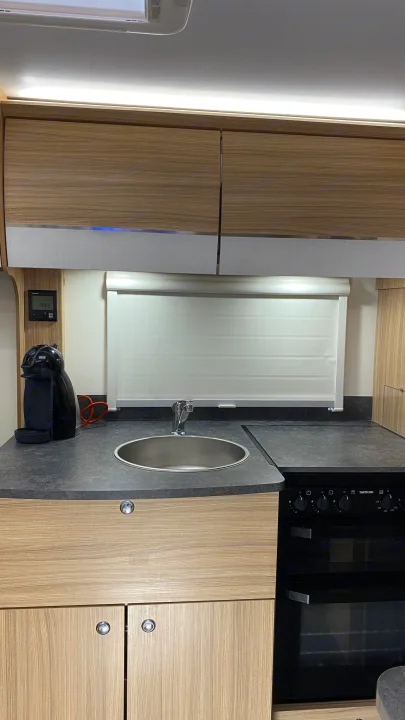 RV rental kitchen showing a compact sink, coffee maker, and oven unit. Overhead cabinets and a window complete the space.. Bailey Pheonix 640 2022