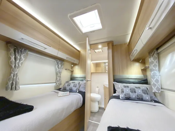 Bright RV rental interior: Twin beds, overhead storage, ambient lighting, and a compact bathroom. Perfect for comfortable journeys.. Bailey x 2022