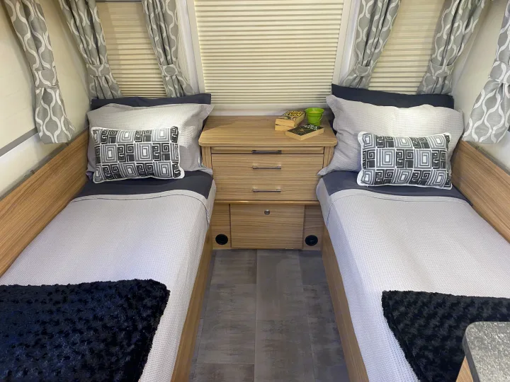 Cozy RV rental twin bedroom featuring two beds, nightstand, patterned curtains, and inviting bedding for a compact stay.. Bailey x 2022