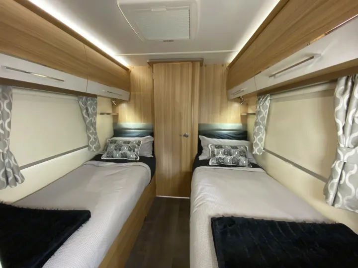 Spacious twin beds in an RV rental bedroom feature modern wood accents, overhead storage, and soft ambient lighting.. Bailey x 2022