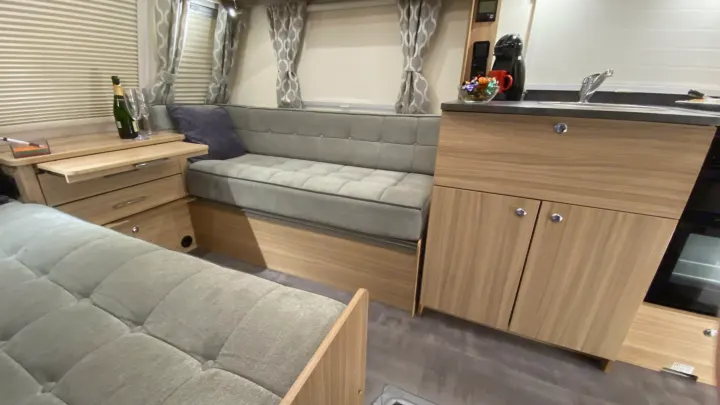 This inviting RV rental interior features comfortable seating, wood-tone cabinetry, a compact kitchen, and champagne ready for celebration.. Bailey x 2022
