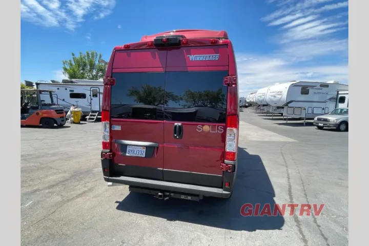 Rear view of a red Winnebago Solis camper van for RV rental, parked at a dealership lot under a blue sky.. Winnebago Solis 2022