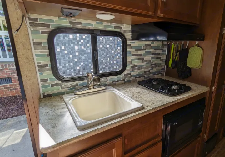 Compact RV kitchen with sink, two-burner stovetop, microwave, and mosaic tile backsplash. Ideal for any rv rental.. Sonic Lite 2016