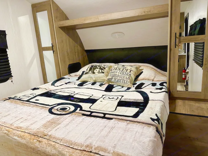 Cozy RV rental bedroom with camper-themed bedding, built-in storage, and warm overhead lighting.. Heartland Pioneer BH270 2023