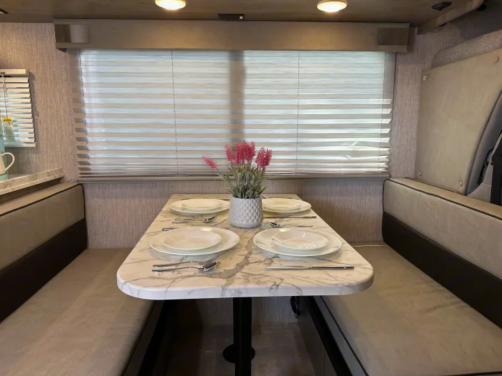 This modern RV rental interior features a comfortable dinette area with a marble table, set for four, perfect for travel.. Forest River Coachmen Freelander 2022