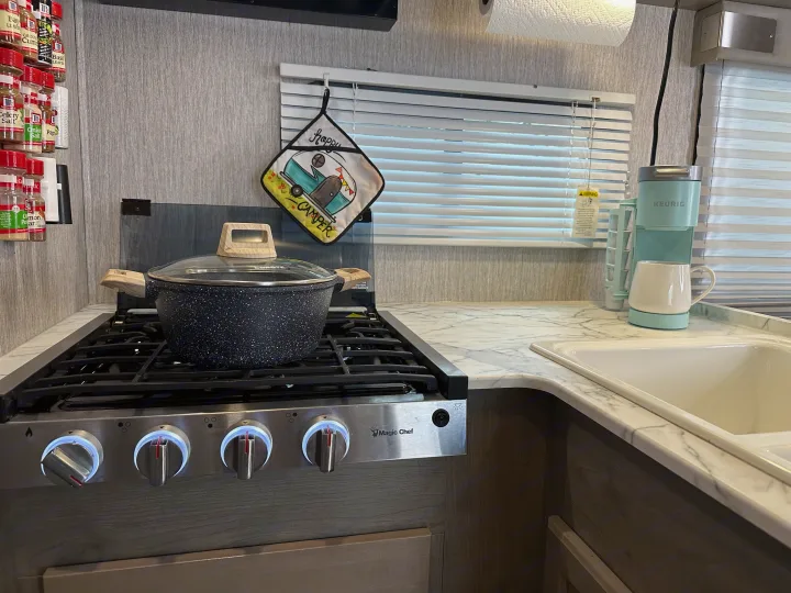 Compact RV rental kitchen featuring a stove with a pot, spice rack, and Keurig, ideal for meals on the go.. Forest River Coachmen Freelander 2022
