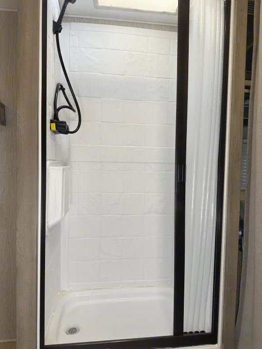 Clean shower stall in an RV rental, featuring a handheld showerhead, storage caddy, and translucent sliding door.. Forest River Coachmen Freelander 2022