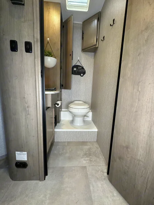 Clean RV rental bathroom: features a compact toilet on a raised step, small vanity, and a cheerful 'Happy Camper' sign.. Forest River Coachmen Freelander 2022