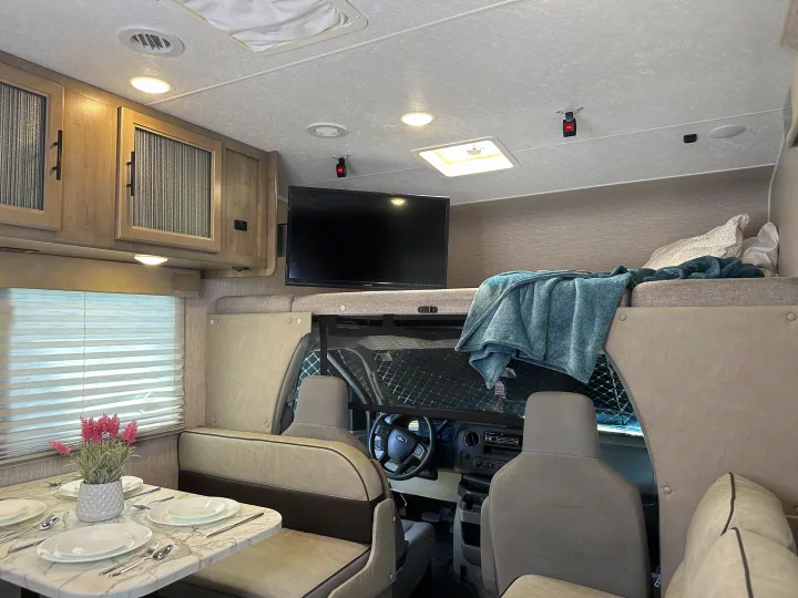 Cozy RV rental interior: dining area with set table, overhead bunk, and front cab for comfortable travel.. Forest River Coachmen Freelander 2022