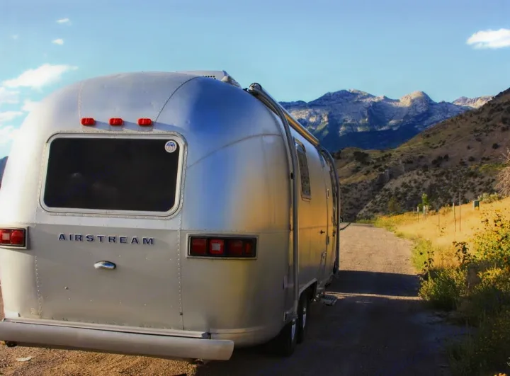 A stunning silver Airstream travel trailer RV rental, parked on a scenic dirt road with mountains beyond.. Airstream Trade Wind 1976